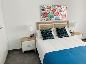 A bedroom with a bed, two bedside tables, a nightstand, a wall-mounted painting, and a door.