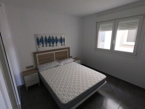 Un dormitorio con cama, mesita de noche, una obra de arte en la pared y ventana.