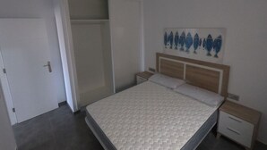 A bedroom with a bed, a nightstand, a bedside table, a wardrobe, and a wall with a fish painting.