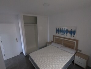 A bedroom with a bed, a nightstand, a bedside table, a wardrobe, and a wall with a fish painting.