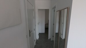 A hallway with white walls, a tiled floor, and a door leading to a room.