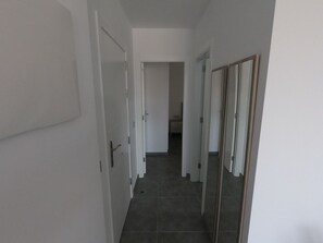 Un pasillo con paredes blancas, suelo de baldosas y una puerta que da a una habitación.