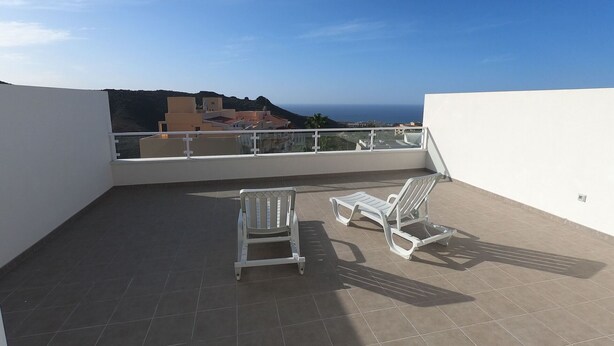 A rooftop terrace with two white lounge chairs and a view of the sea and buildings.
