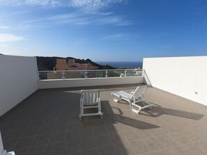 En takterrass med två vita loungestolar och utsikt över havet och byggnaderna.