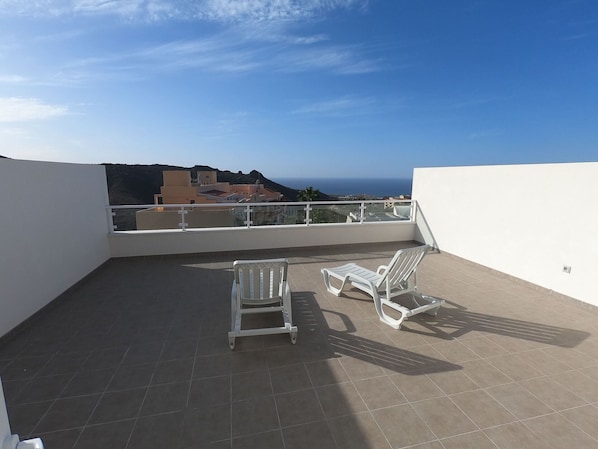 Una terraza en la azotea con dos sillones blancos y vistas al mar y edificios.
