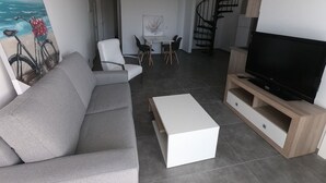 A modern living room with a sofa, a coffee table, a TV, and a dining area with chairs and a table.