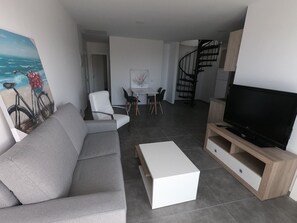 Un salon moderne comprenant un canapé, une table basse, un téléviseur et un coin repas avec des chaises et une table.