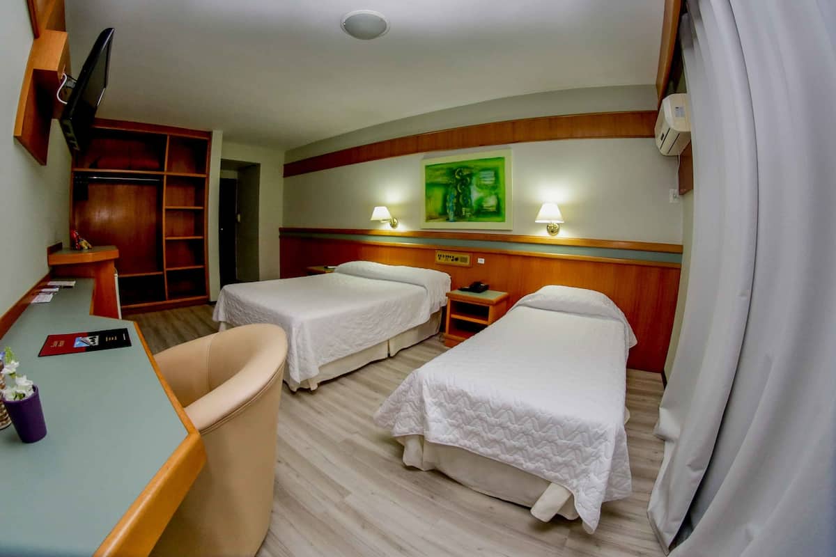 Une chambre d’hôtel avec deux lits, un bureau, une chaise, une télévision et un tableau au mur.