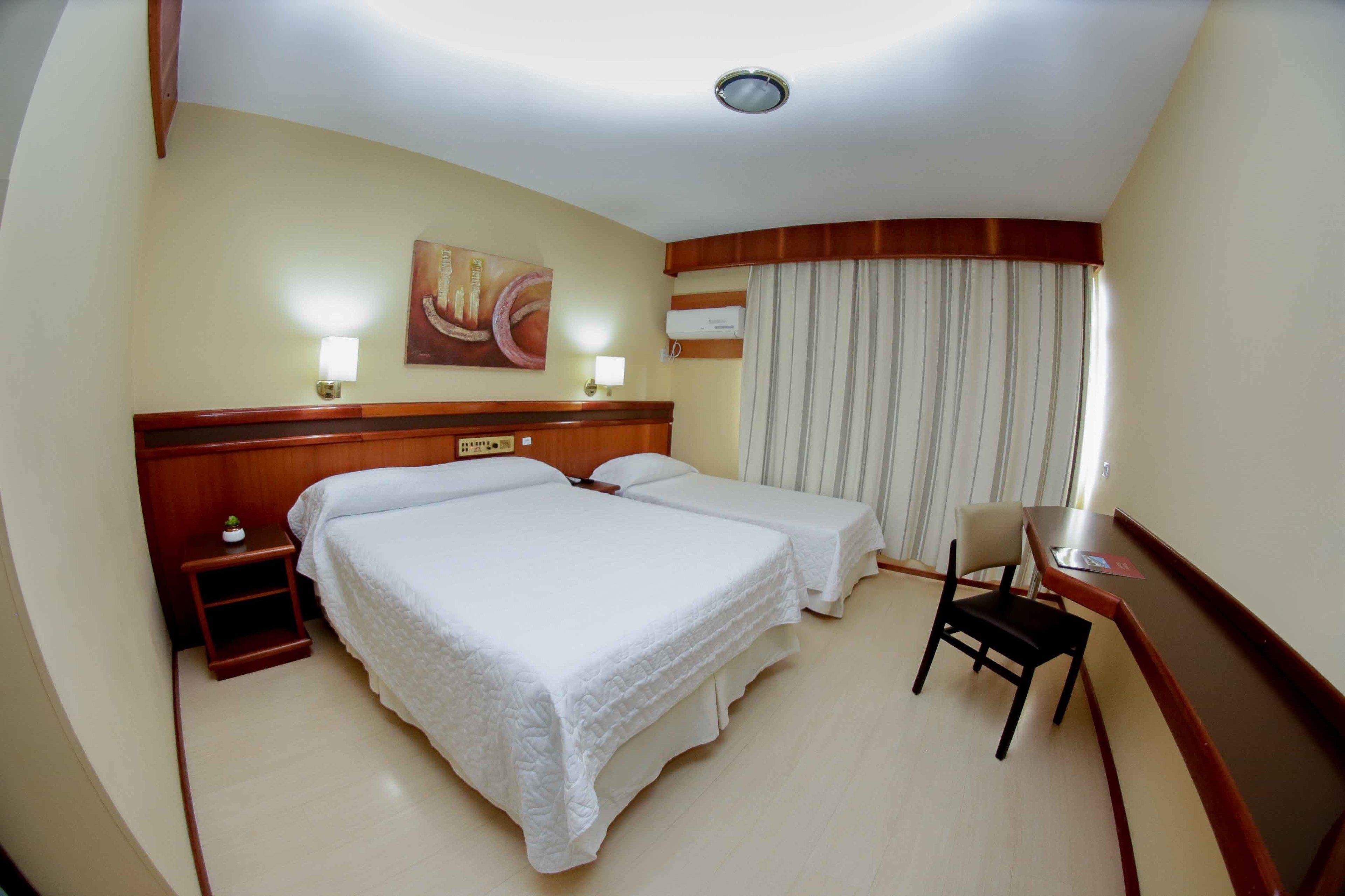 A hotel room with two beds, a desk, a chair, a small table, and a painting on the wall.