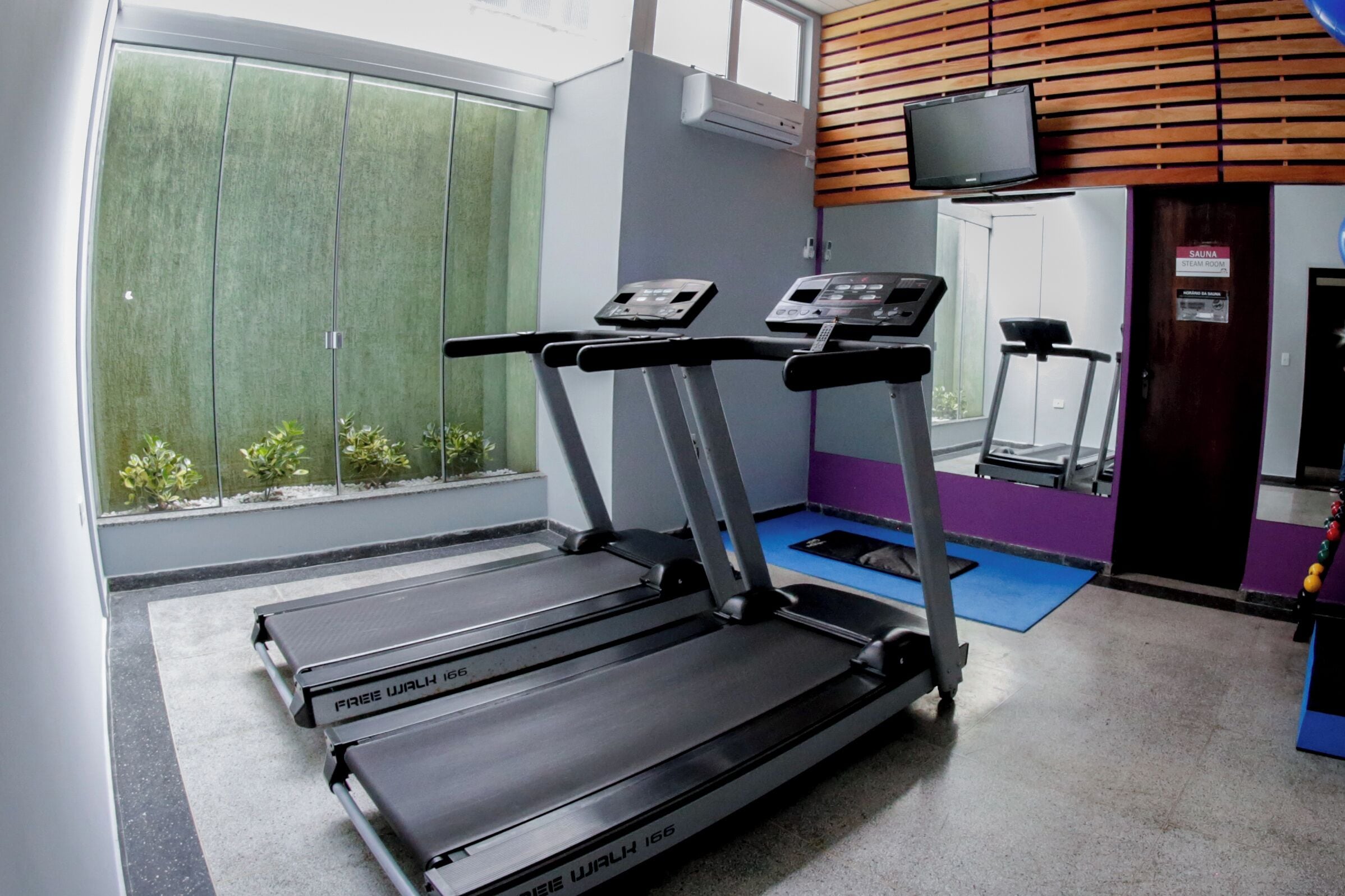 Un gimnasio con cintas de correr, sauna y un televisor en la pared.