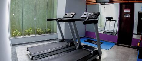 Un gimnasio con cintas de correr, sauna y un televisor en la pared.
