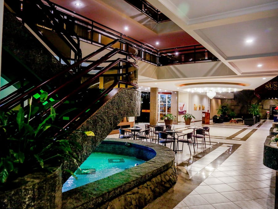 Un vestíbulo de hotel con piscina central, una escalera y zonas de estar.
