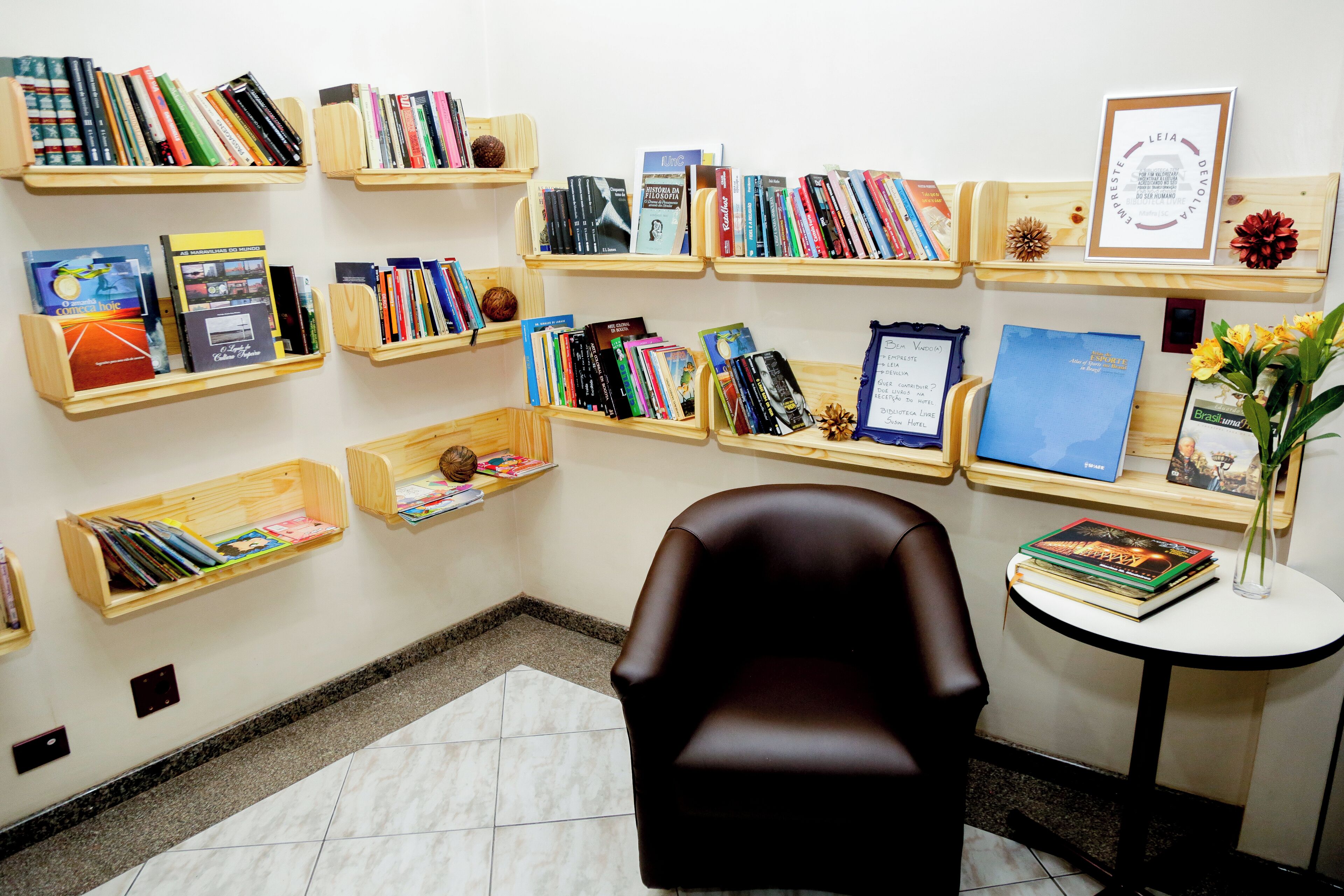 Un rincón de lectura con varias estanterías de madera llenas de libros, un sillón de cuero y una mesita con un florero.