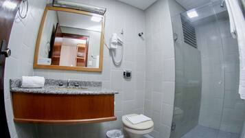 A bathroom with a granite countertop, a wooden vanity, a toilet, a glass-enclosed shower, and a mirror with a light above it.