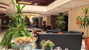 A hotel lobby with a high ceiling, glass railings, and a seating area with a sofa and chairs. - Susin Hotel (Mafra)