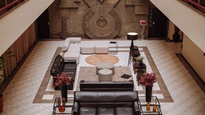 A spacious lobby with a modern design, featuring a large seating area with sofas and a coffee table, a decorative wall with geometric patterns, and a staircase with a red railing. - Susin Hotel (Mafra)