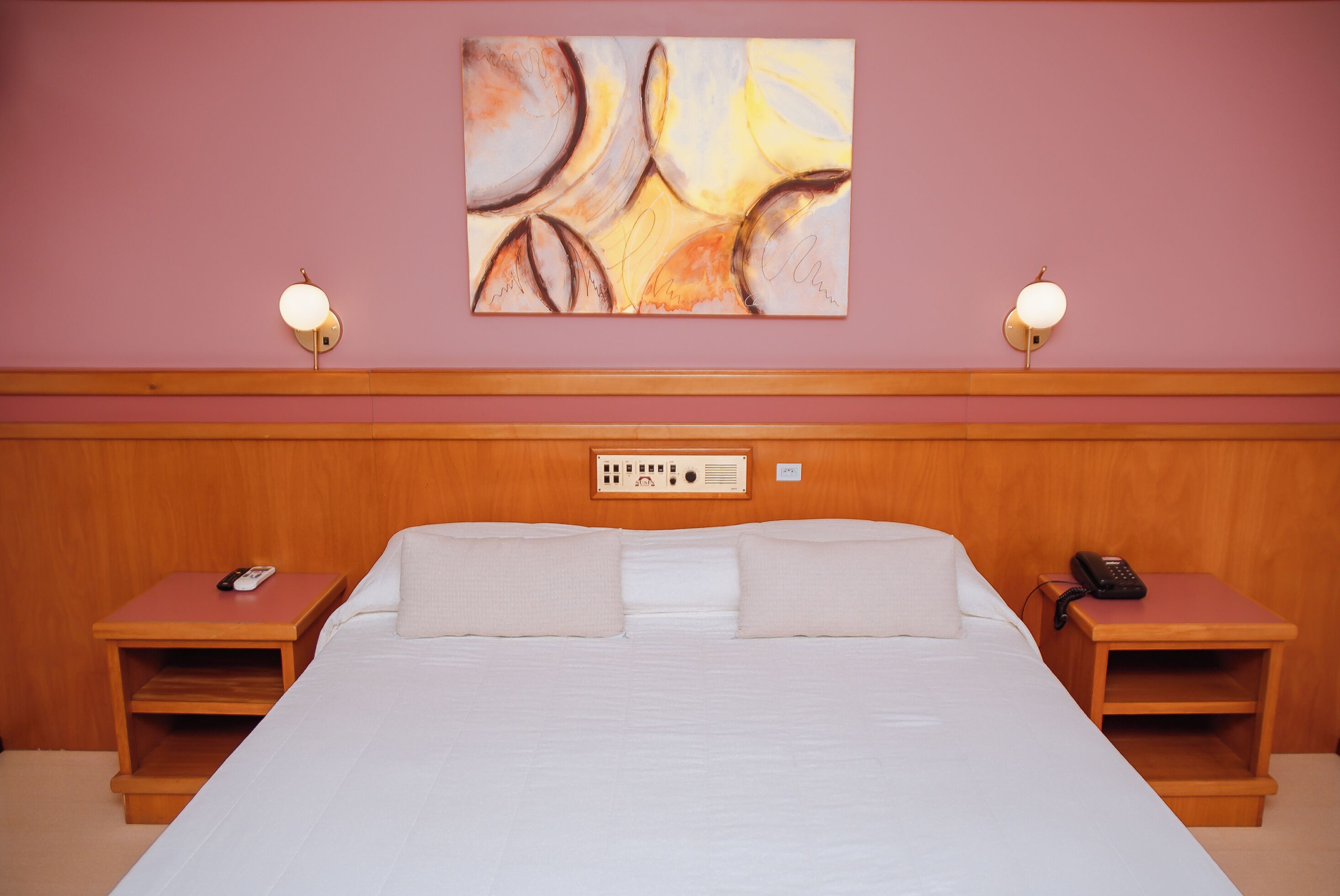 A hotel room with a large bed, two bedside tables with lamps, a wall-mounted artwork, and a wooden headboard.