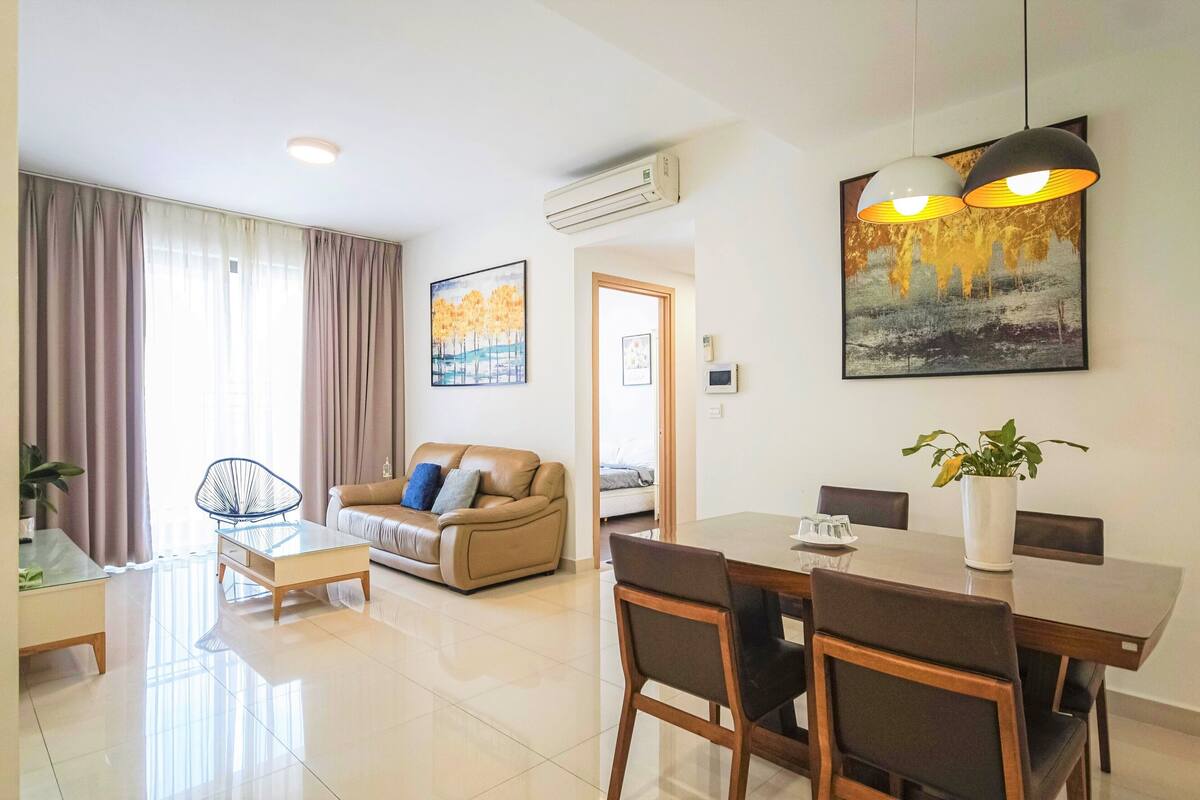 A modern living room with a sofa, coffee table, dining table with chairs, and artwork on the walls.
