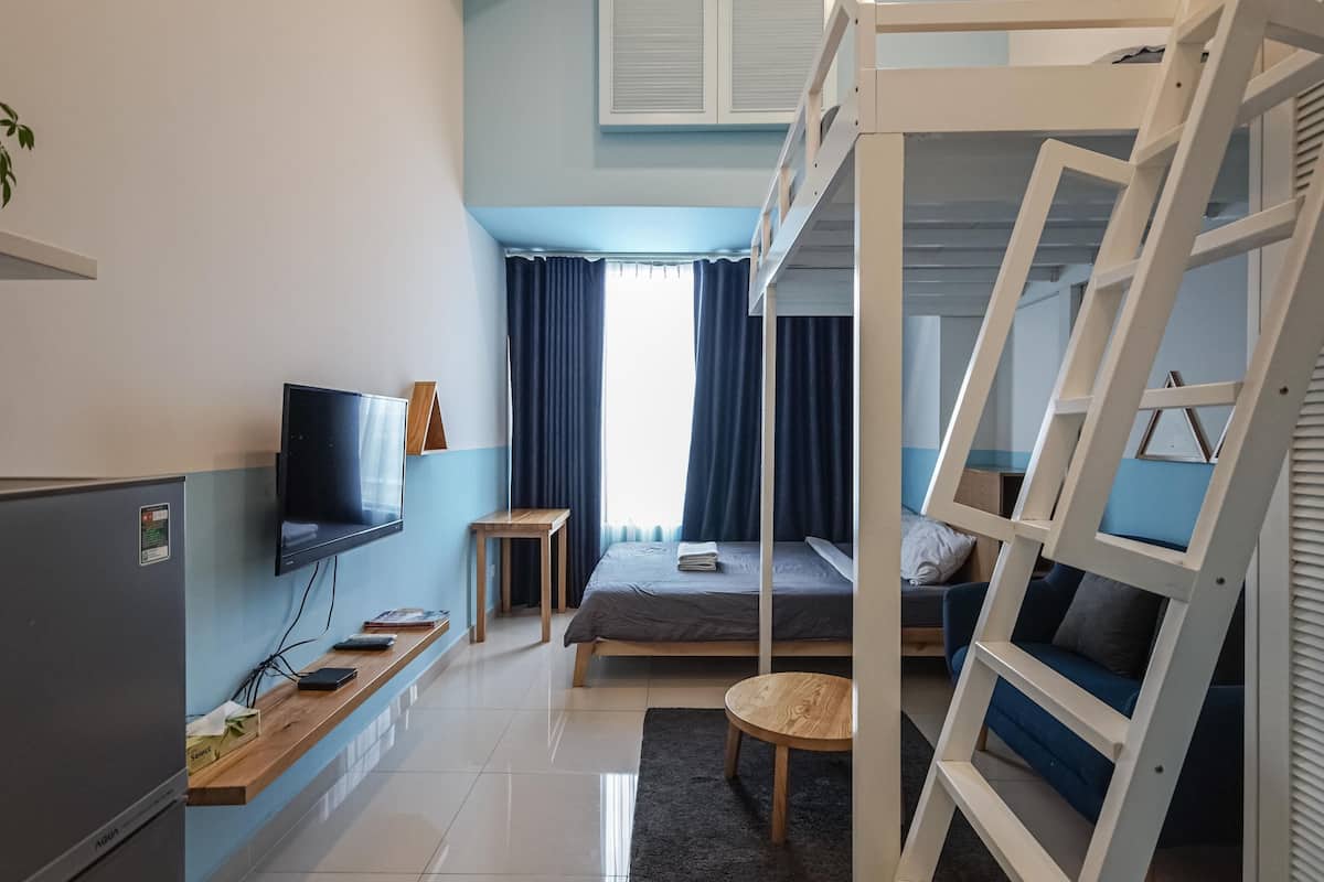 A compact room with a bunk bed, a flat-screen TV mounted on the wall, a small wooden table, and a desk with a computer.