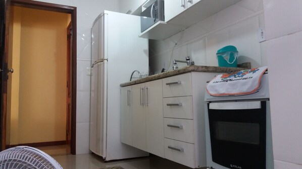 Cozinha compacta com geladeira, micro-ondas, pia e forno pequeno.