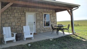 Una casa de dos pisos con fachada de piedra, un porche cubierto con mobiliario exterior y vistas a un campo cubierto de césped.