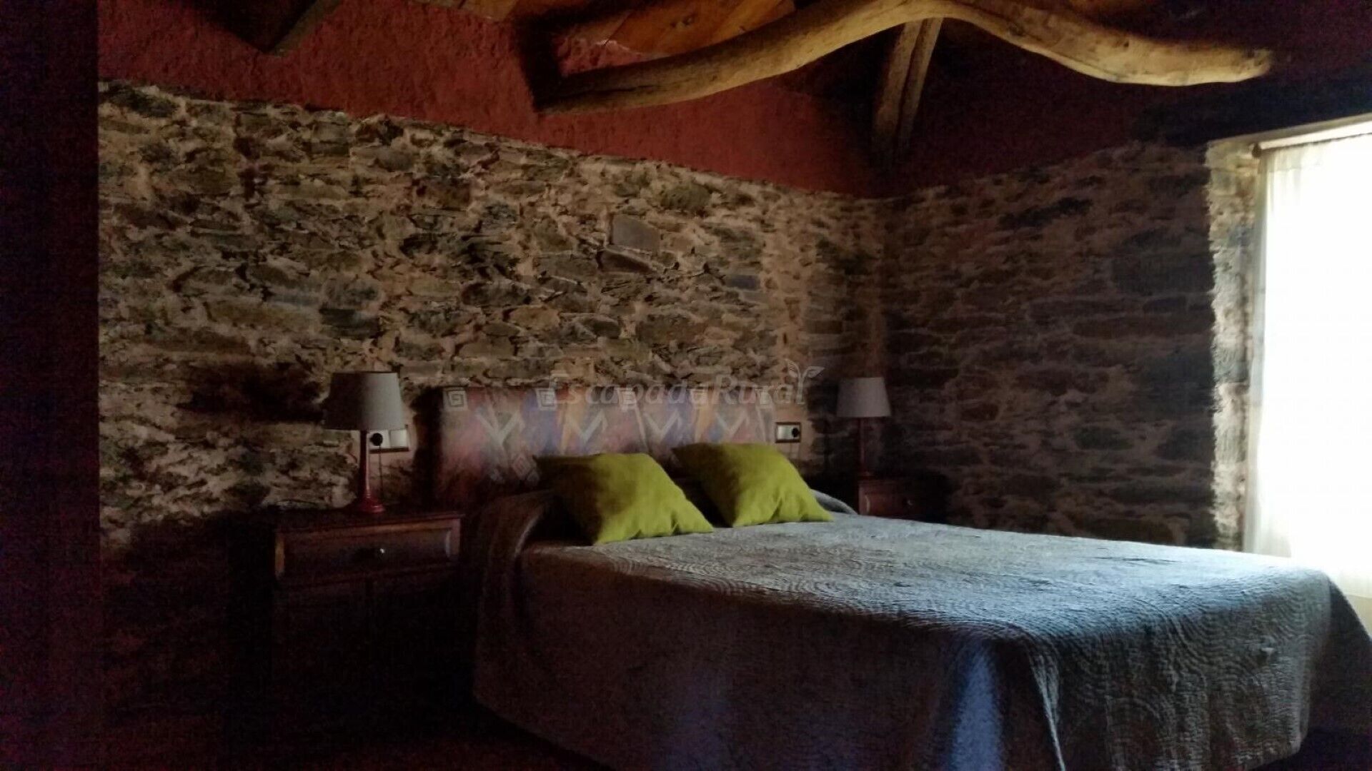Una camera rustica con parete in pietra, un letto con cuscini verdi e due lampade ai comodini.