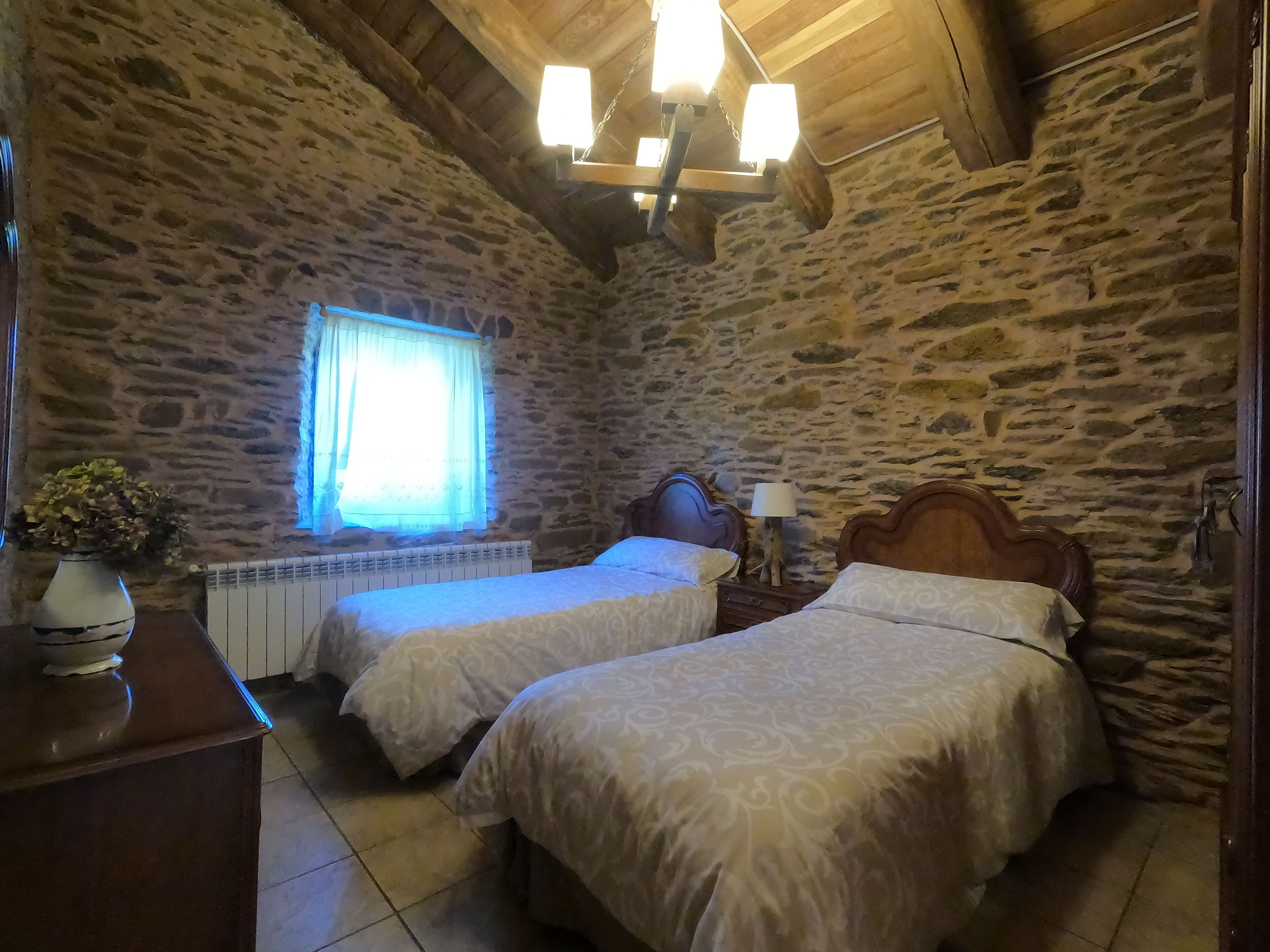 Una stanza con pareti in pietra, due letti con copriletto decorato, un poggiatesta in legno, un comodino con una lampada e un termosifone.