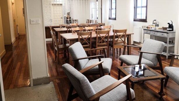 A spacious room with wooden tables and chairs, a glass-top table, and a kitchenette area.