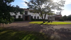 A large, white building with a red-tiled roof, surrounded by well-maintained lawns and trees.