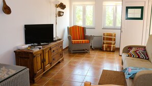 Un salon avec une télévision, un fauteuil, un canapé et une fenêtre.