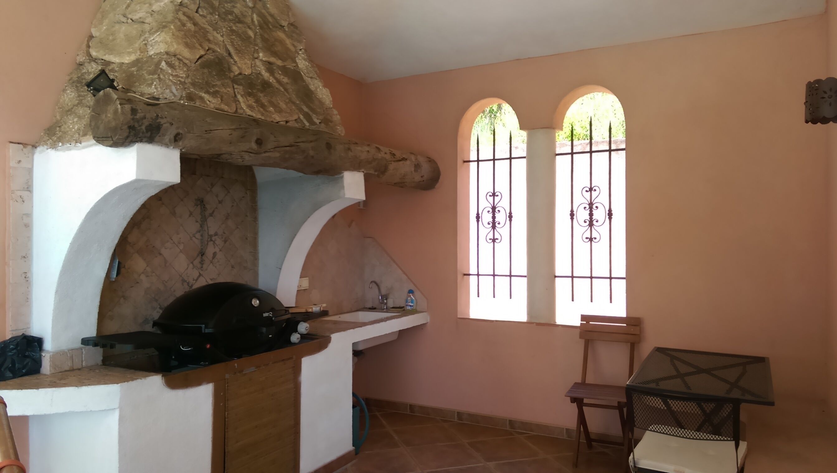 A kitchen with a stone chimney, a sink, and a window with decorative bars.