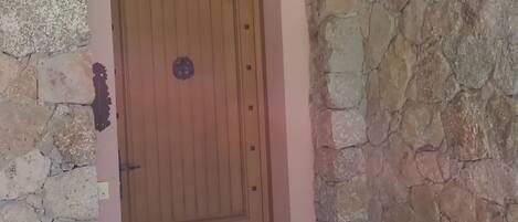 A stone-walled entrance with a wooden door, a small shelf, and tiled flooring.