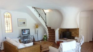 Un salon avec une cheminée, un téléviseur, des meubles en osier et un escalier.