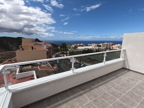 A balcony with a view of a coastal town, a tiled floor, and a white railing.