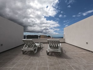 Une terrasse sur le toit avec deux chaises longues, une vue sur l’océan et un ciel dégagé.