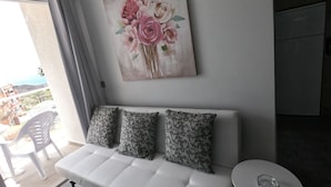 A modern living room with a white sofa, two patterned cushions, a small round table, and a floral artwork on the wall.