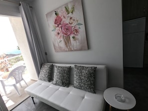 A modern living room with a white sofa, two patterned cushions, a small round table, and a floral artwork on the wall.