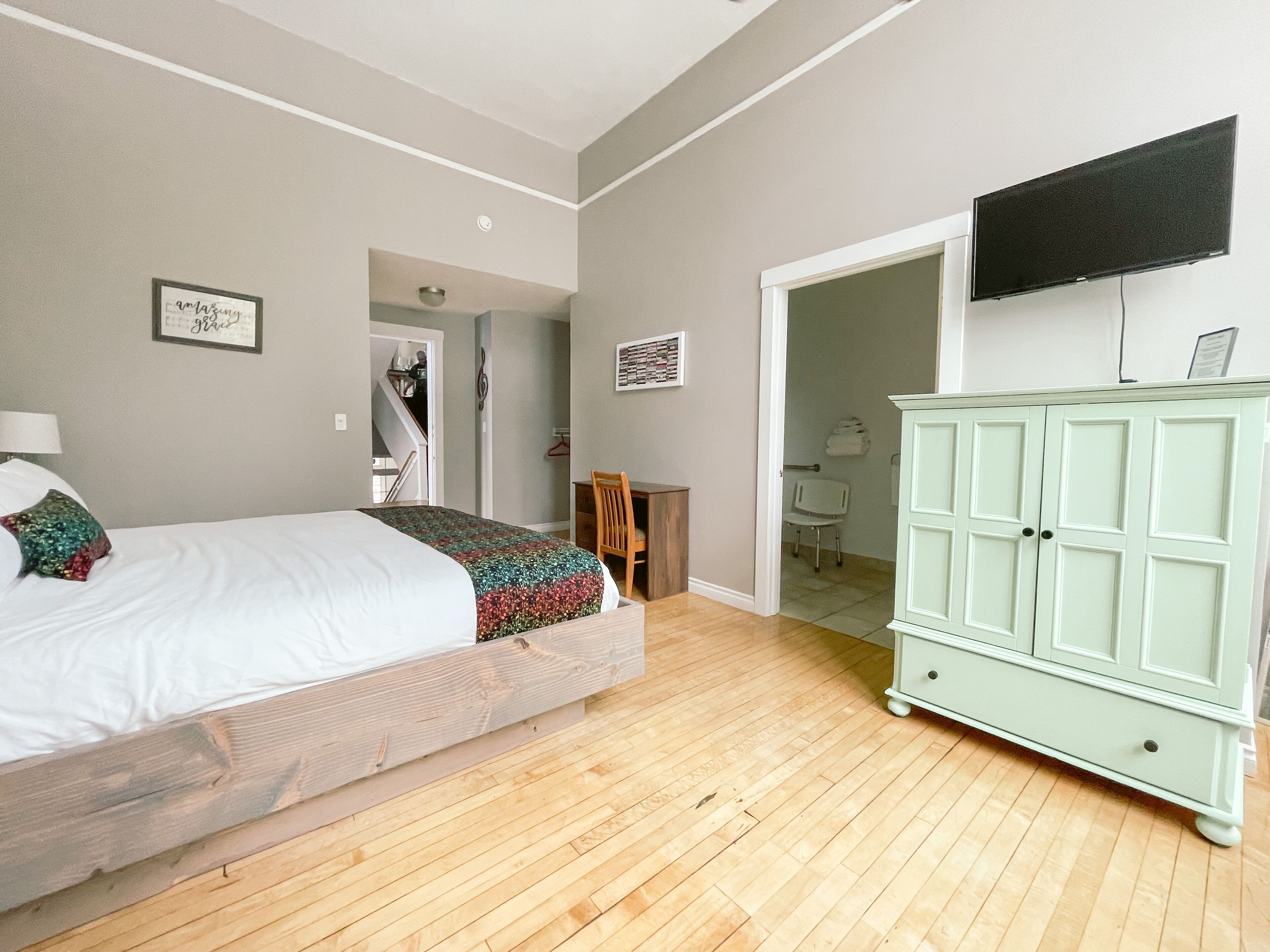 Un dormitorio con cama, armario, televisión y puerta al baño.
