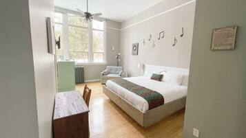 Un dormitorio con cama, escritorio, silla, radiador y ventana con vistas a árboles.