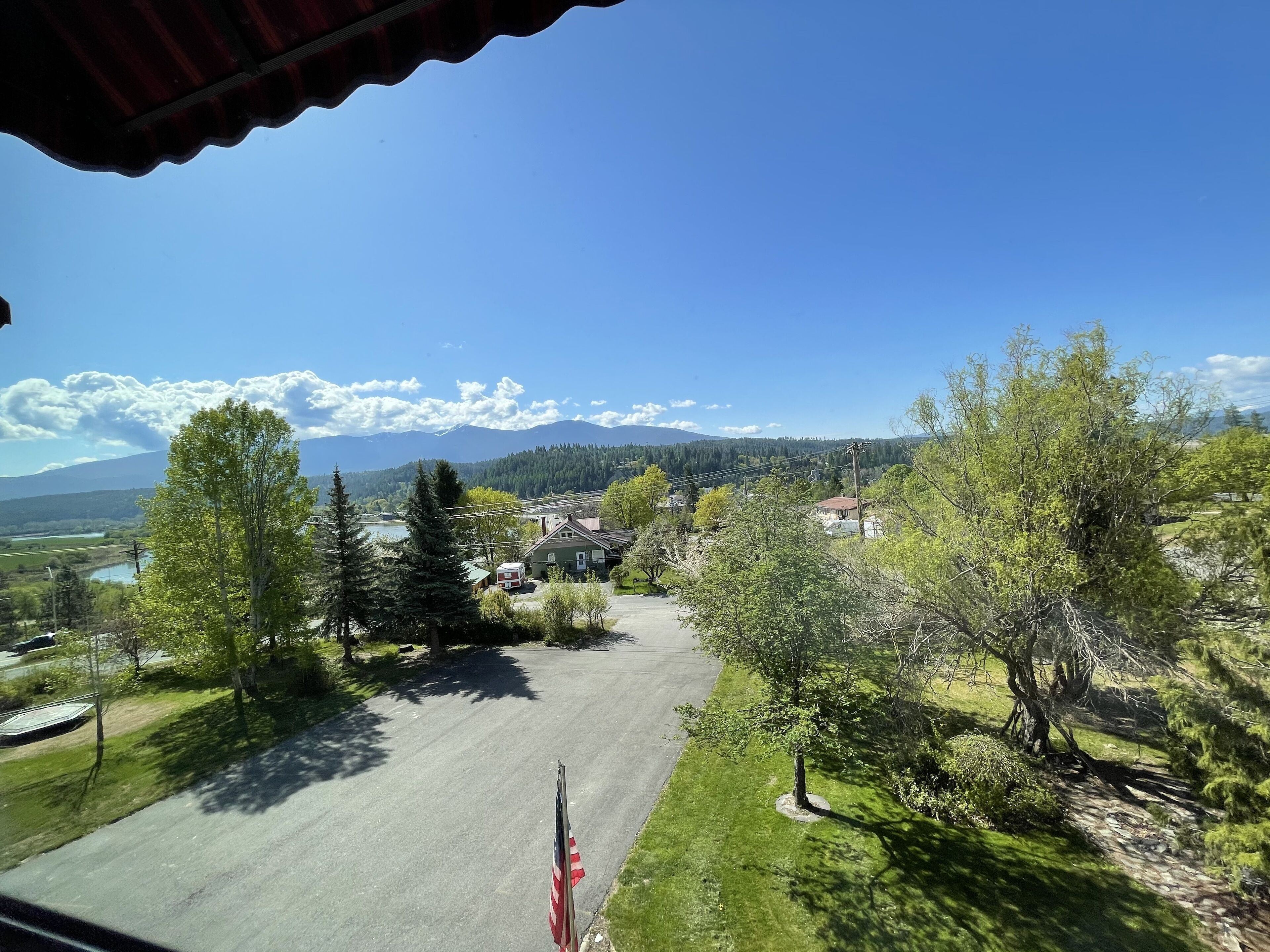 A view from a window overlooking a road with trees and houses, with mountains in the background.