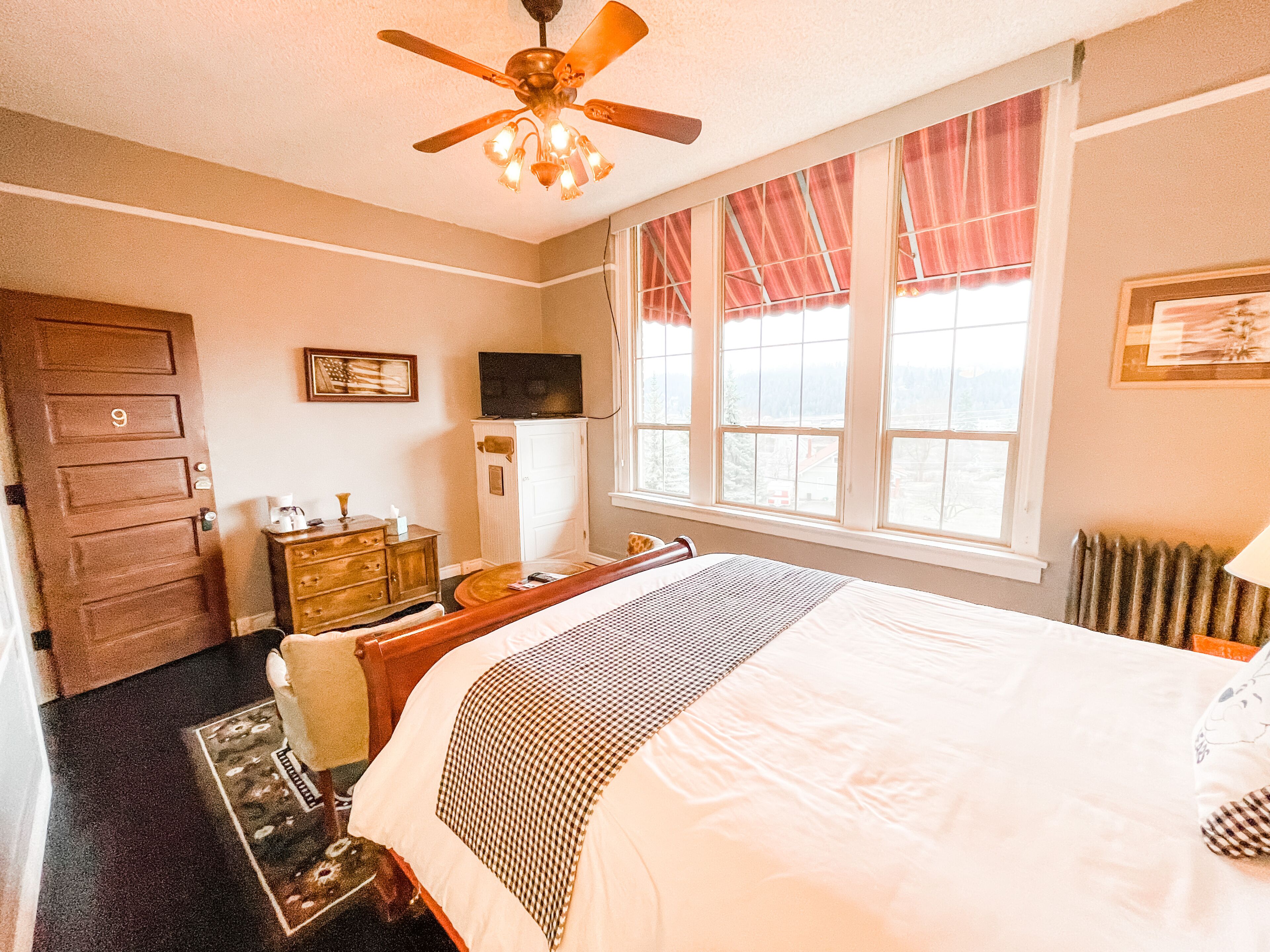 Een hotelkamer met een bed, een bureau, een dressoir, een televisie en een raam met gordijnen.
