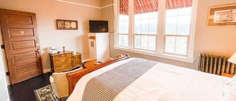 Een hotelkamer met een bed, een bureau, een dressoir, een televisie en een raam met gordijnen.