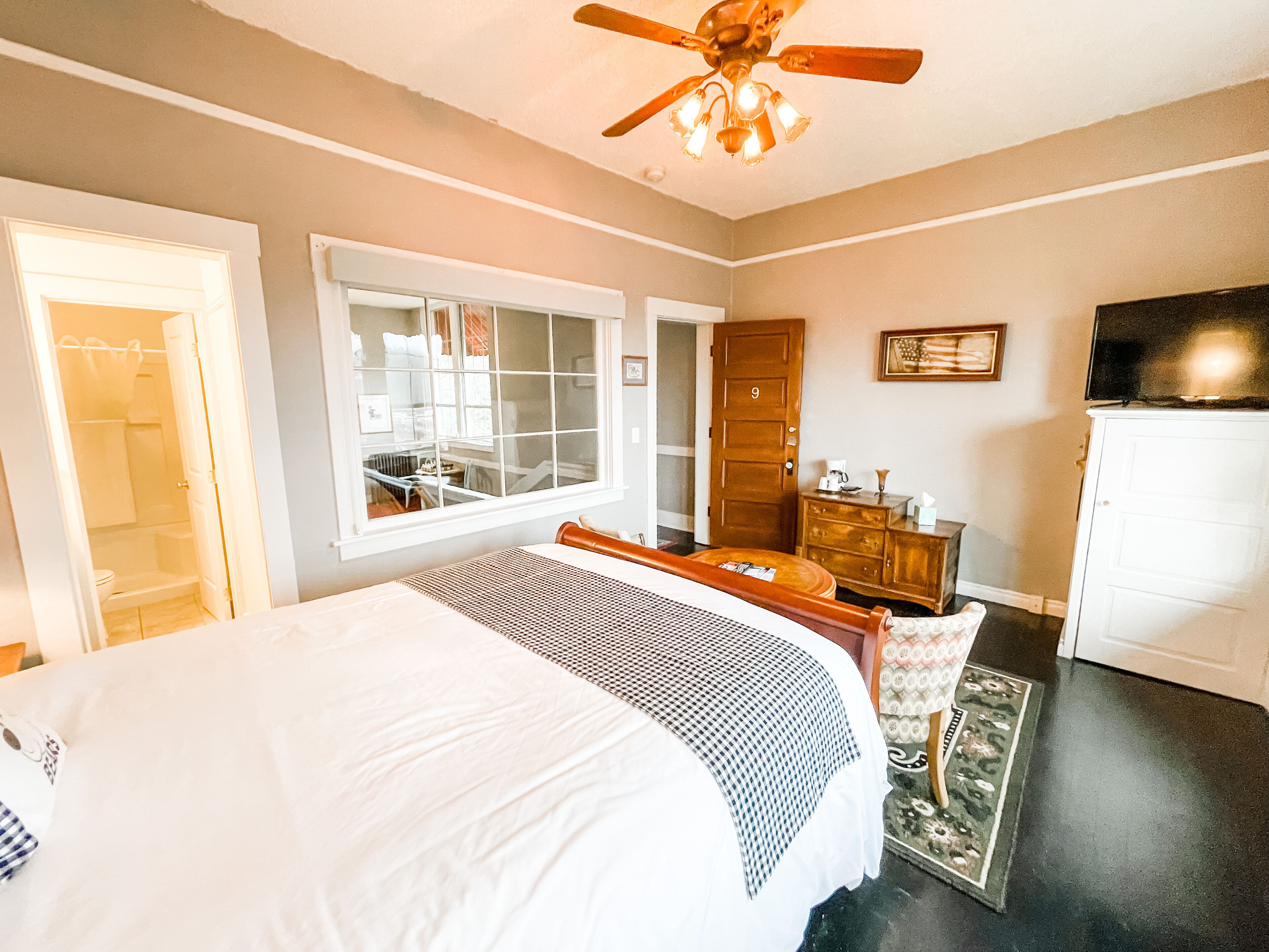 A bedroom with a large bed, a wooden dresser, a vanity, and a ceiling fan.