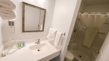 Un baño con lavamanos, espejo, toallero y zona de ducha.