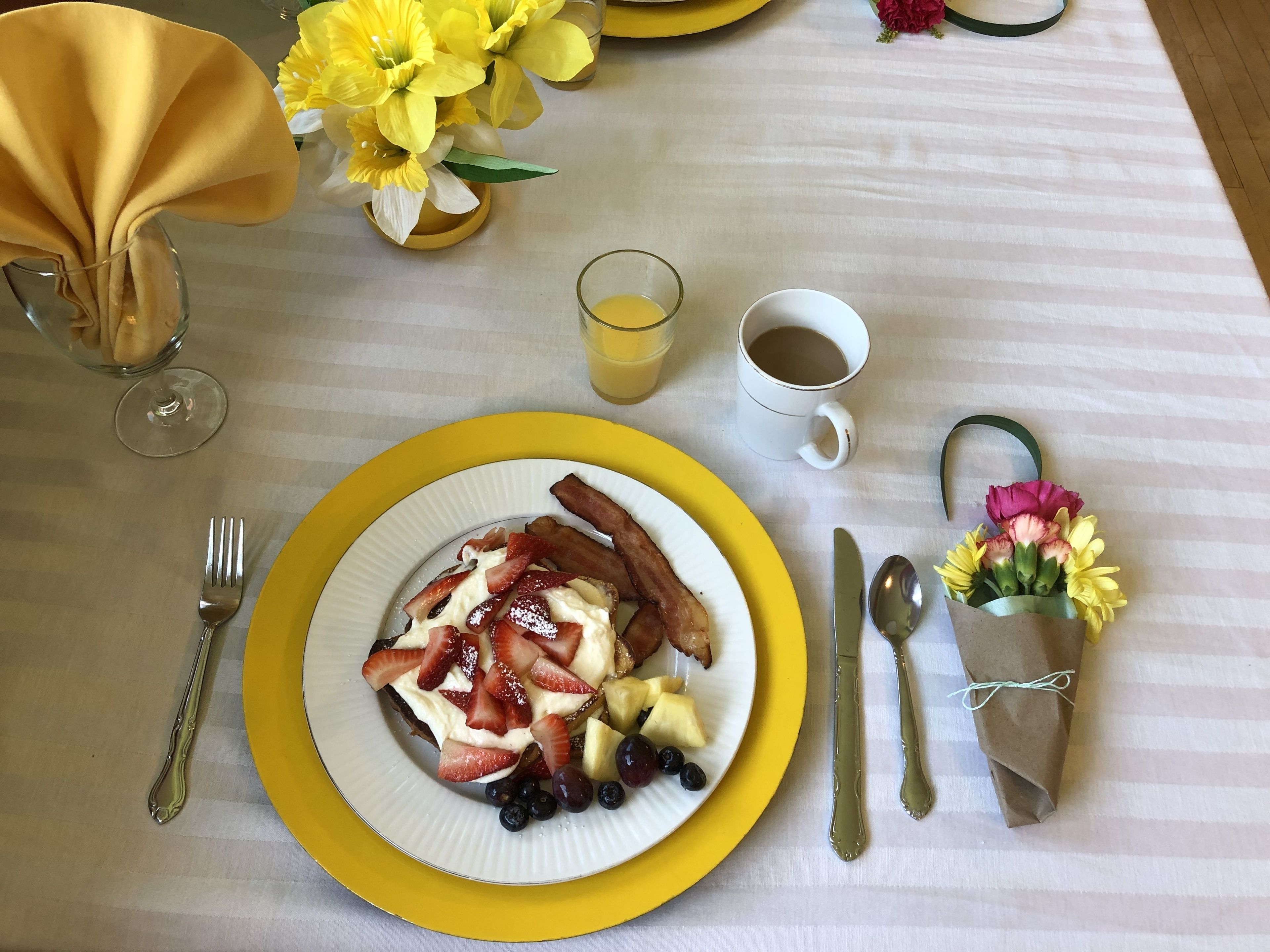 A breakfast setting with a plate of pancakes topped with strawberries, blueberries, and bacon, accompanied by a glass of orange juice and a cup of coffee.