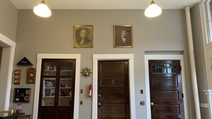 A hallway with three wooden doors, a coat rack with hats, a wall clock, and a framed portrait. - Northside School B&B (Bonners Ferry)