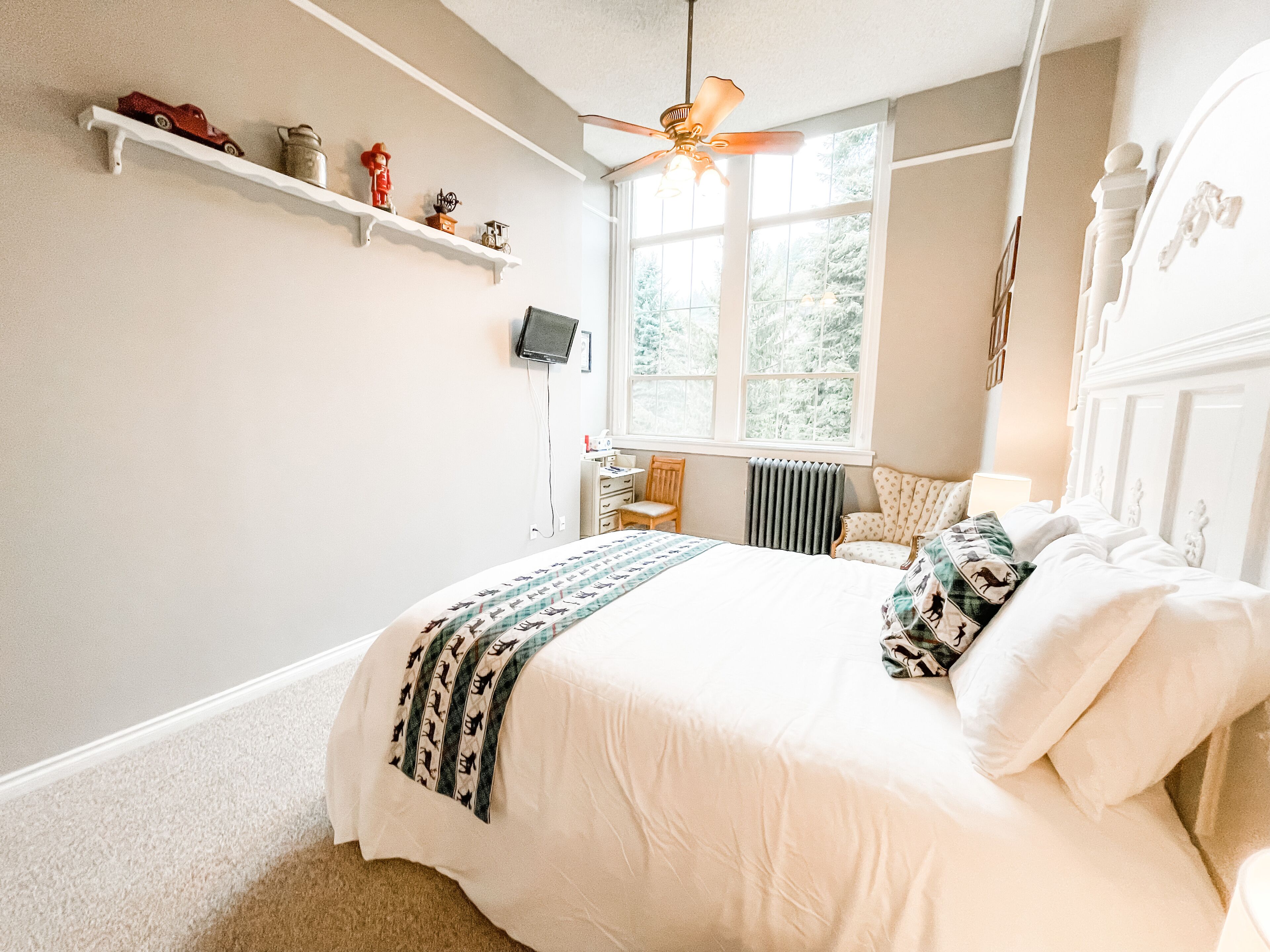 Una camera da letto con un letto, una ventola a soffitto, una finestra e uno scaffale con oggetti decorativi.