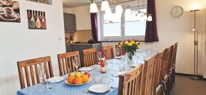 Un coin repas avec une table dressée pour quatre personnes, des chaises en bois, un vase rempli de fleurs et une horloge au mur.