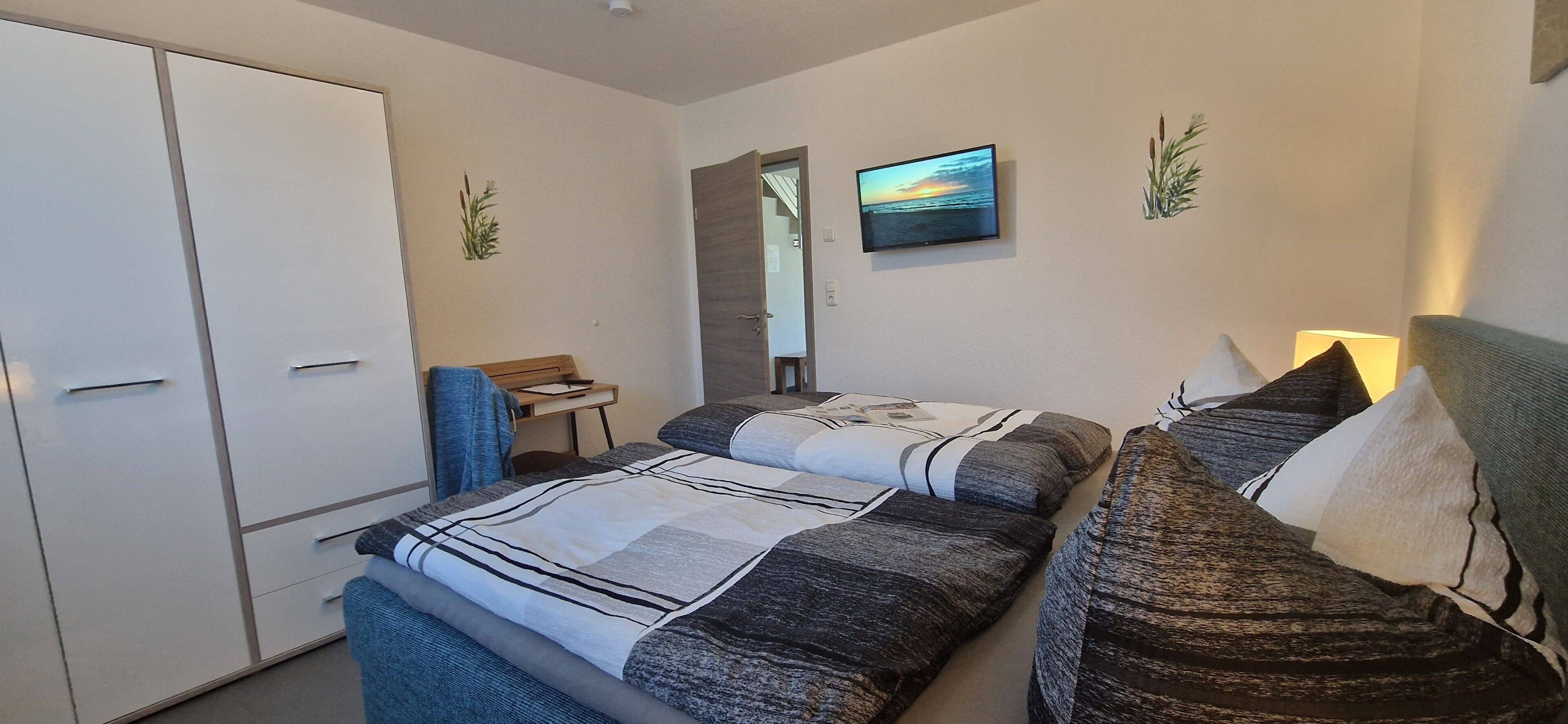 A bedroom with a bed, a desk, a wardrobe, and a television on the wall.
