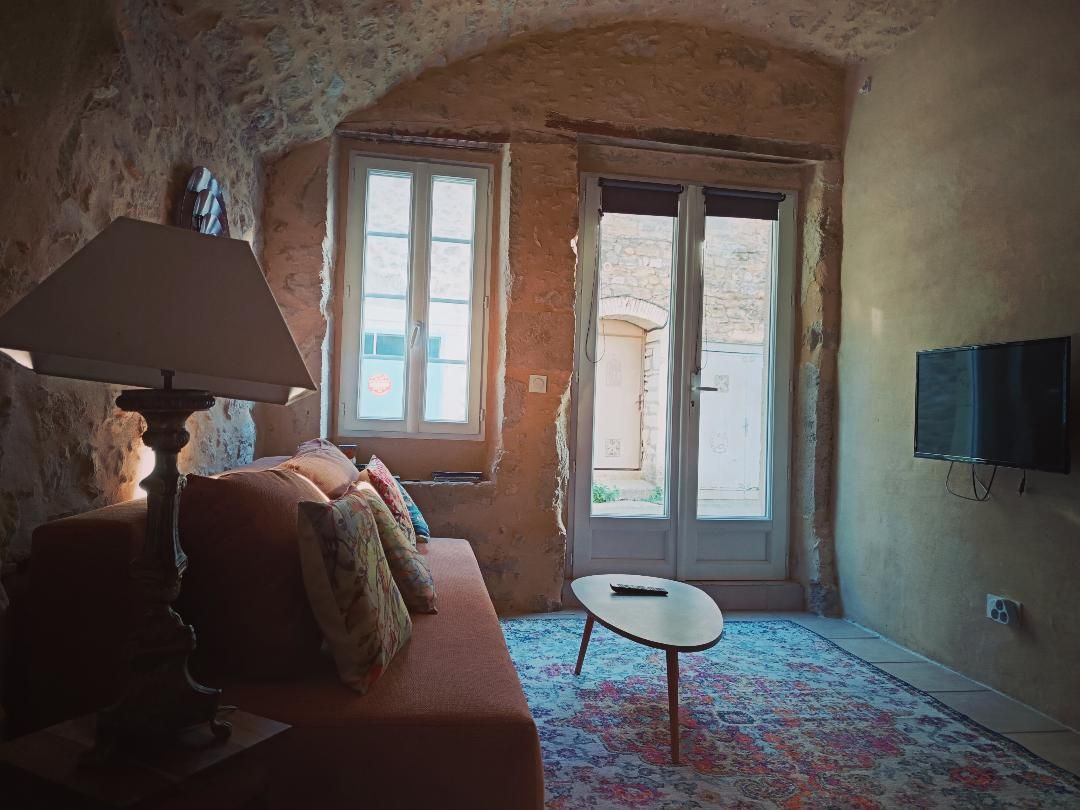 Una habitación con sofá, mesa, lámpara, televisión y puerta que da al exterior.
